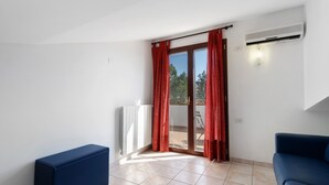 A room with a sliding glass door, a radiator, a blue sofa, and a tiled floor. - Villa Ristòries Room 6 with Terrace, Wi-Fi and Air Conditioning (Matera)