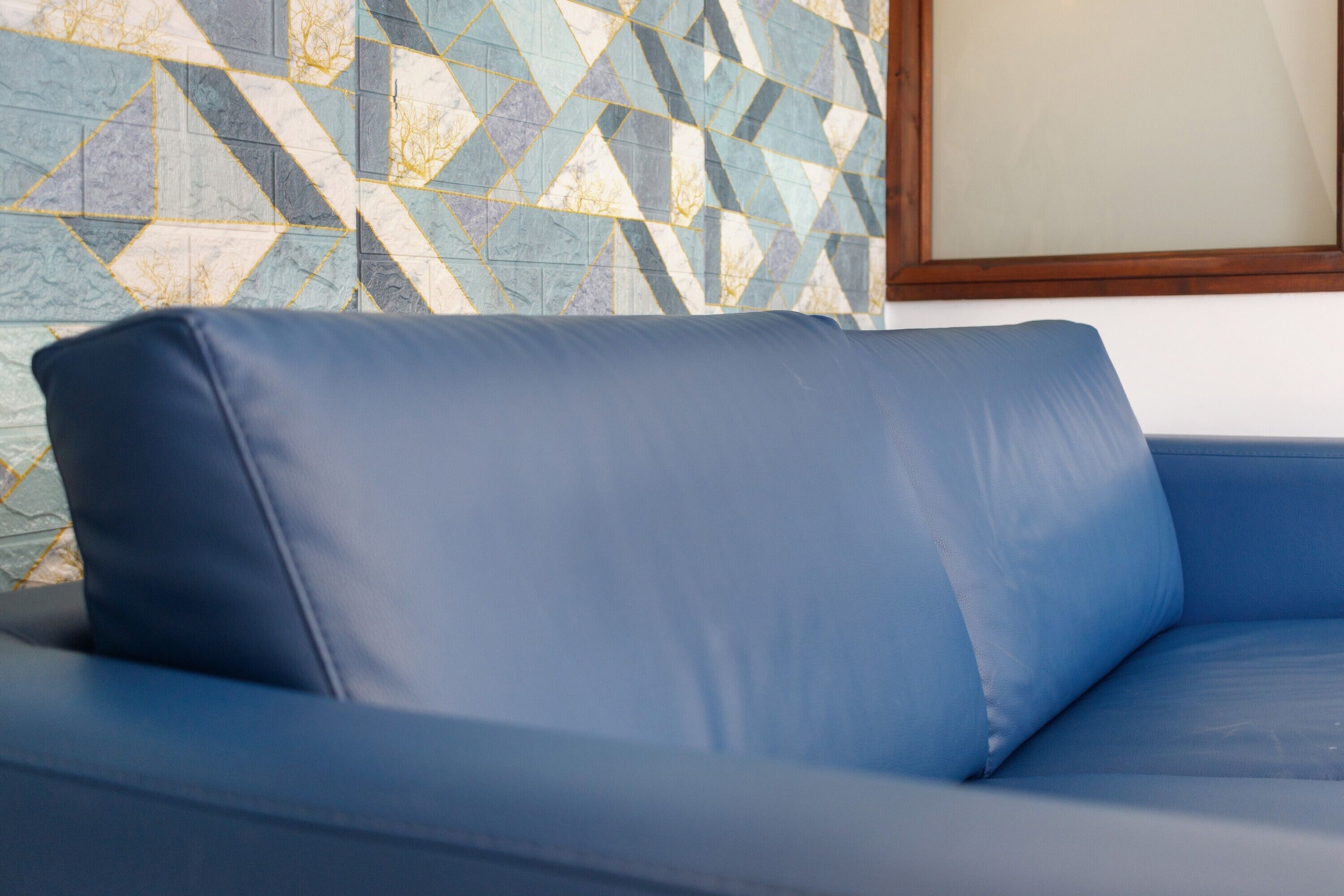 A blue sofa with a cushion in a room with a geometric patterned wall.