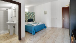 A hotel room with a bathroom, a bed with a blue bedspread, and a wall with a geometric pattern. - Villa Ristòries Room 6 with Terrace, Wi-Fi and Air Conditioning (Matera)