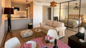 Un appartement moderne comprenant un coin repas avec une nappe à carreaux, une cuisine, un salon avec un canapé et une chambre à coucher avec un lit et une table de chevet.