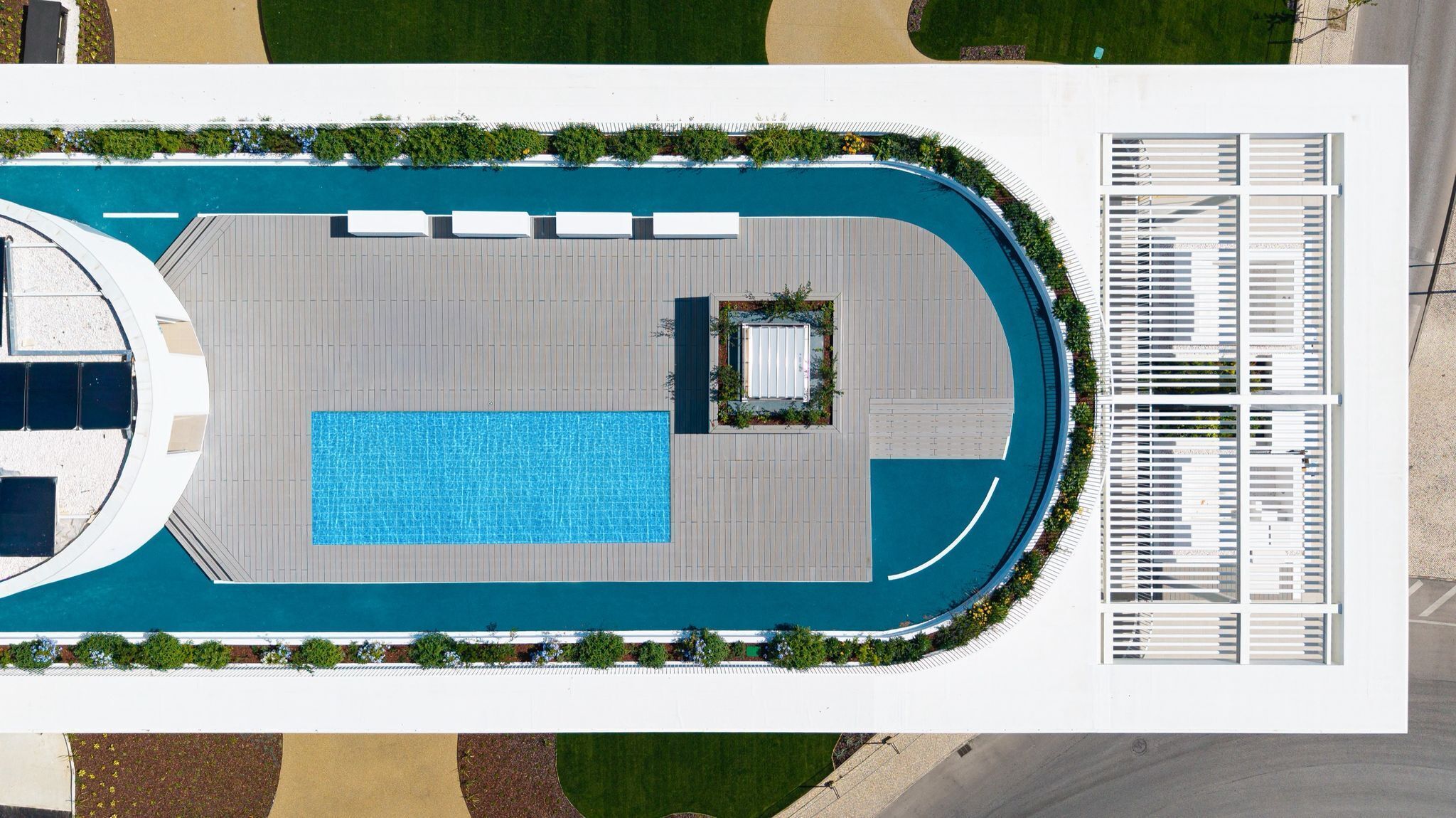 A top-down view of a swimming pool area with a rectangular pool, a sun lounger, and a covered seating area.