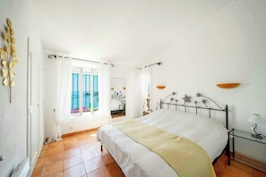 Ein Schlafzimmer mit Bett, Nachttisch, Fenster mit Vorhängen und Blick nach draußen.