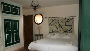 Et soveværelse med en seng, et rundt spejl, en lampe og en væg med et billede af en fugl.