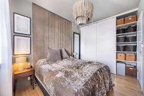 Ein Schlafzimmer mit Bett, Nachttisch, Lampe, Kleiderschrank und Regalen mit Körben.