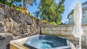 Ein Whirlpool in einer Holzkonstruktion mit Steinwand und Bäumen im Hintergrund.