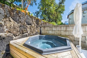 Ein Whirlpool in einer Holzkonstruktion mit Steinwand und Bäumen im Hintergrund.