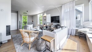 Ein modernes Wohnzimmer mit einer Couch, einem Korbstuhl, einem kleinen Tisch und einem Fernseher.
