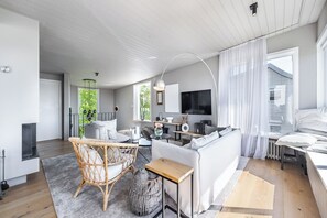 Ein modernes Wohnzimmer mit einer Couch, einem Korbstuhl, einem kleinen Tisch und einem Fernseher.