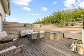 A wooden deck with wicker furniture, a hot tub, and potted plants. - Modern and family friendly house in Reykjavik (Reykjavík)