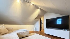 A modern living room with a large flat-screen TV, a sofa, and a carpeted floor. - Modern and family friendly house in Reykjavik (Reykjavík)