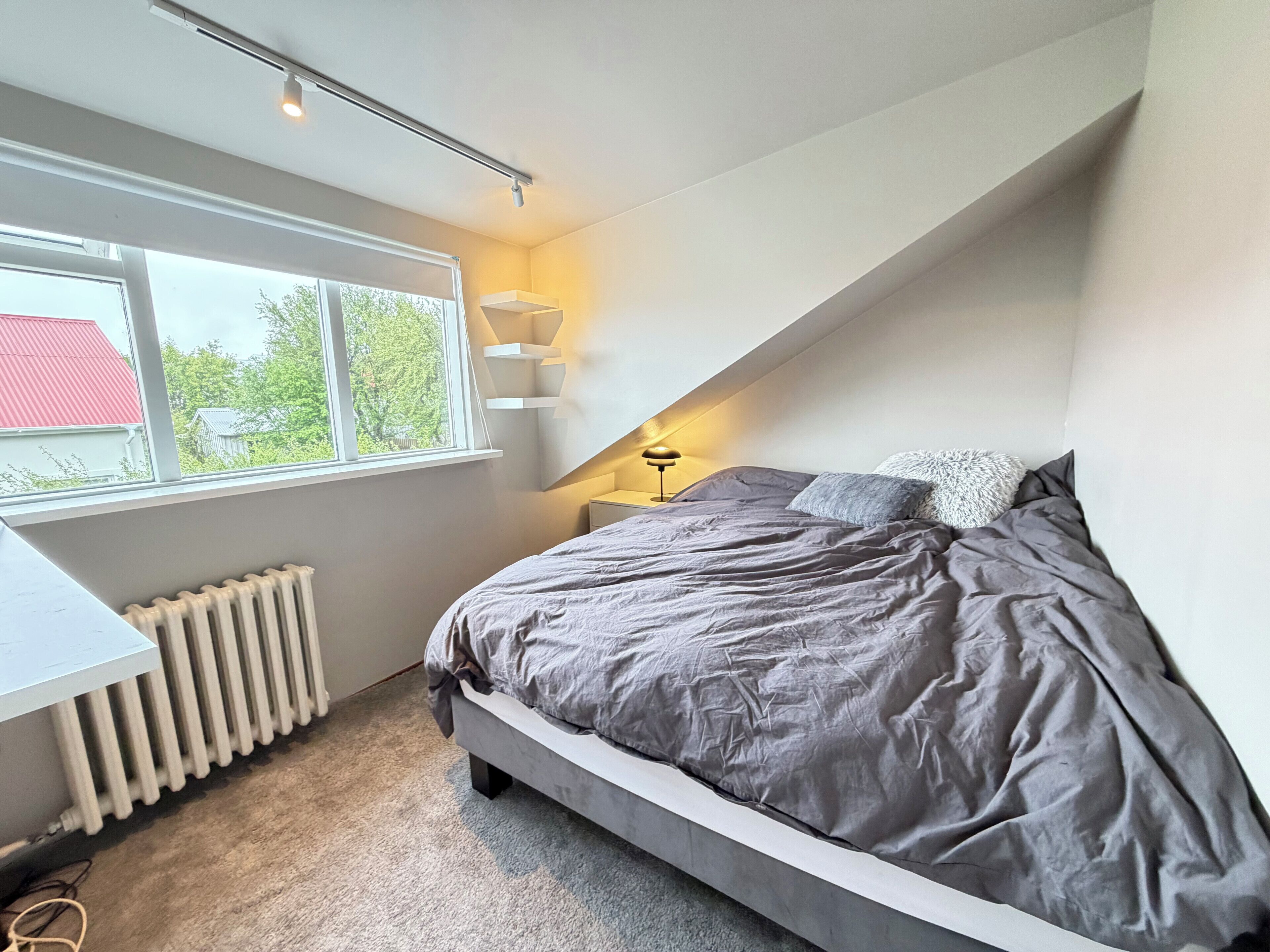 A bedroom with a bed, a window, a radiator, and a lamp.