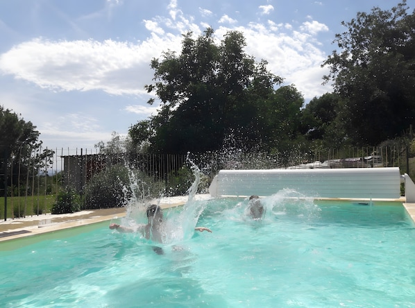 Une piscine à l’eau claire, entourée d’arbres et d’une clôture.