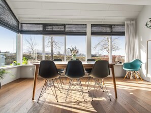 A modern dining area with a wooden table, three chairs, and a view through large windows. - Modern and family friendly house in Garðabær (Garðabær)