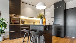 Ett modernt kök med en inbyggd ugn, en diskho och en bardisk med barstolar.