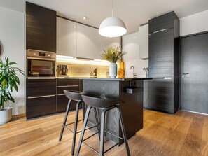 A modern kitchen with a built-in oven, a sink, and a bar area with stools. - Modern and family friendly house in Garðabær (Garðabær)