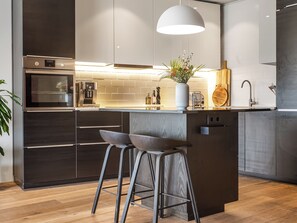 A modern kitchen with stainless steel appliances, a central island with stools, and a pendant light. - Modern and family friendly house in Garðabær (Garðabær)