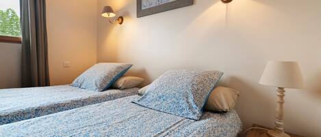 A hotel room with two beds, a nightstand, a lamp, and a wall-mounted picture.
