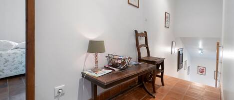 A room with a bed, a desk with a lamp, and a chair. There are framed pictures on the wall.