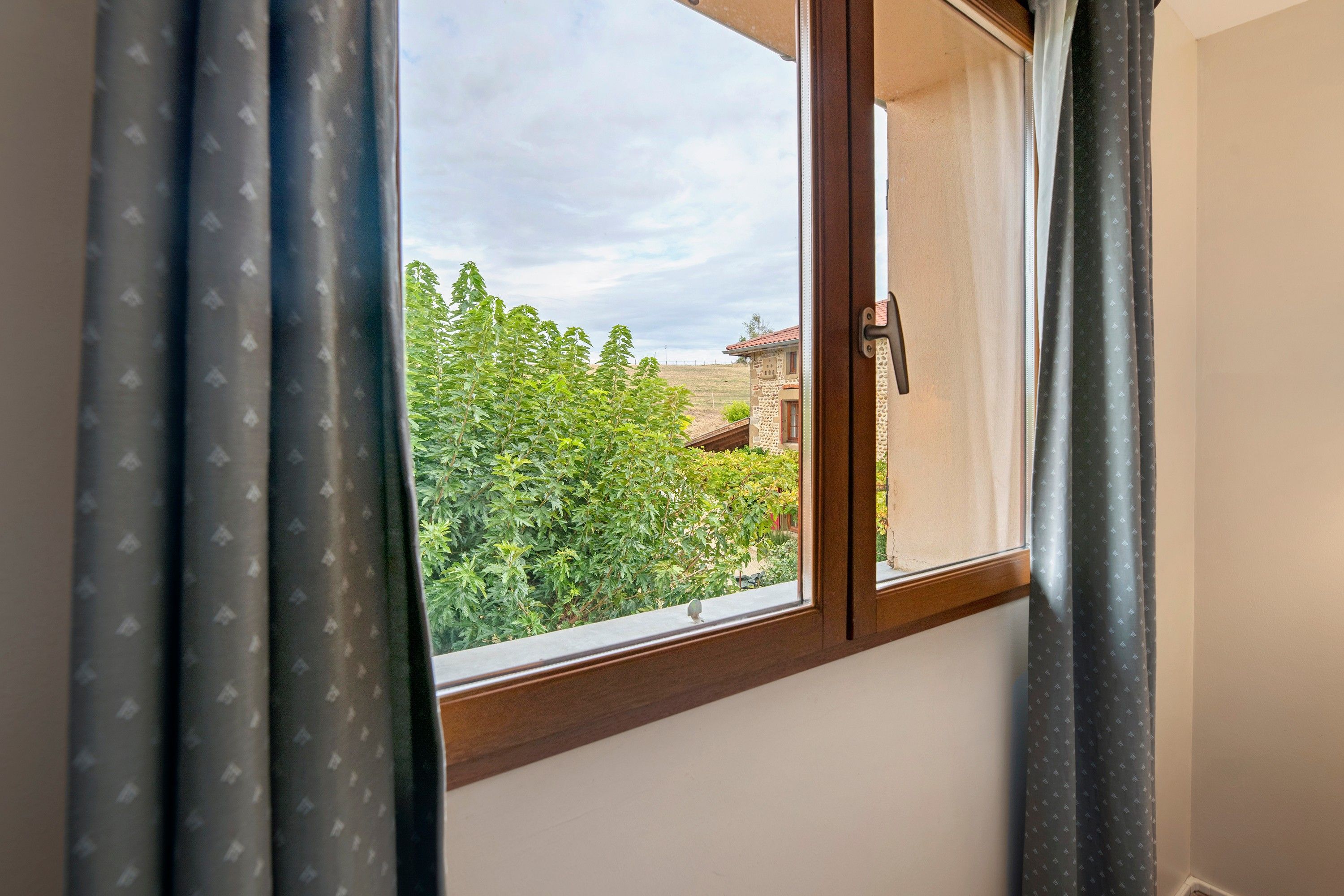 Una ventana con vista a un paisaje verde y un edificio de techo rojo.
