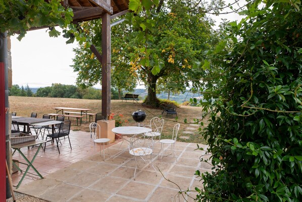 An outdoor patio with tables and chairs, a barbecue grill, and a view of the surrounding landscape.