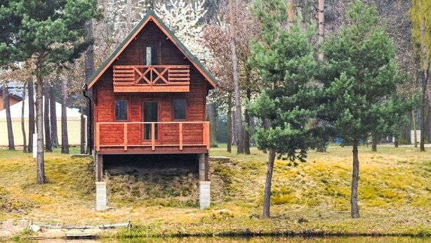 A wooden cabin with a balcony, surrounded by trees and a body of water. - Cosy apartment in villa for 6 people with A/C, WIFI, TV, patio and pets allowed (Dvůr Králové Nad Labem)