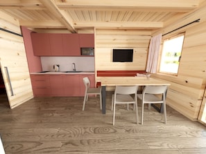 Eine kompakte Holzhütte mit Küchenzeile, einem Essbereich mit Stühlen und einem Fenster mit Vorhängen.