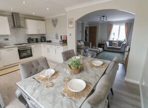 Una cocina moderna con armarios blancos, una mesa de comedor de mármol y vistas a una sala de estar con un sofá y una ventana.
