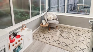 Un solárium con vista a un jardín trasero, una kitchenette pequeña y un sillón gris con cojín.