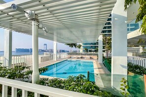 Una piscina en la azotea con vistas al horizonte de la ciudad, rodeada de vegetación y arquitectura moderna.