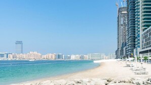 Una playa con el horizonte de una ciudad al fondo, incluyendo edificios altos y una torre.