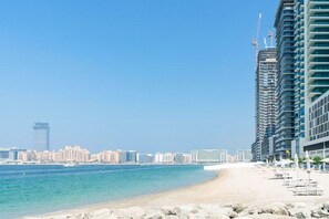 A beach with a city skyline in the background, including high-rise buildings and a tower. - Luxury Beachfront 1 BED Apartment in Dubai Harbor (Dubai)
