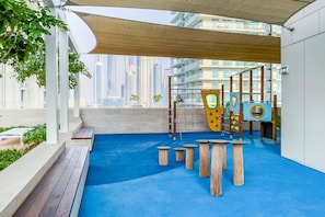 Un área de juegos al aire libre con piso azul, bancos de madera y equipo infantil.