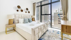 Un dormitorio moderno con una cama grande, una mesita de noche, una lámpara, una obra de arte en la pared y vistas de un paisaje urbano a través de amplias ventanas.