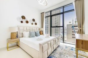 Un dormitorio moderno con una cama grande, una mesita de noche, una lámpara, una obra de arte en la pared y vistas de un paisaje urbano a través de amplias ventanas.
