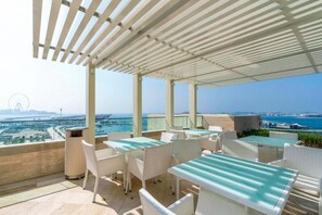 Una terraza en la azotea con mesas al aire libre, vista al mar y una noria a lo lejos.