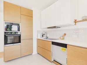Eine moderne Küche mit Holzschränken, einem eingebauten Backofen, einer Kaffeemaschine und einem Geschirrspüler.