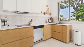 Een moderne keuken met witte kasten, een vaatwasser, een koffiezetapparaat en een raam met uitzicht op bomen.