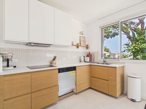 Eine moderne Küche mit weißen Schränken, einem Geschirrspüler, einer Kaffeemaschine und einem Fenster mit Blick auf Bäume.
