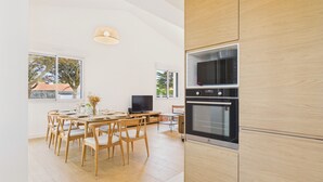 Een moderne keuken met houten kastjes, een eettafel met stoelen, een televisie en een groot raam.