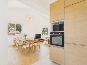 Eine moderne Küche mit Holzschränken, einem Esstisch mit Stühlen, einem Fernseher und einem großen Fenster.