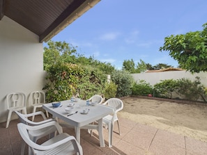 Eine Terrasse mit Tisch und Stühlen, umgeben von Pflanzen und einer weißen Mauer.