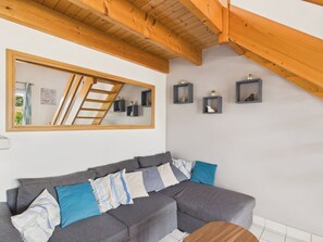 Ein modernes Wohnzimmer mit einem grauen Ecksofa, einer Holzbalkendecke und einem großen Spiegel.