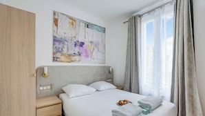 Un letto rifatto con lenzuola bianche, un lampadario a parete e un grande quadro astratto sopra.