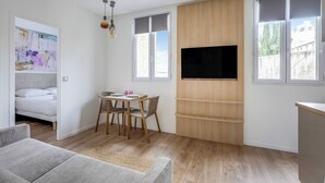 Un soggiorno moderno con una TV a schermo piatto, scaffali in legno, un'area pranzo con sedie e un'ampia finestra.