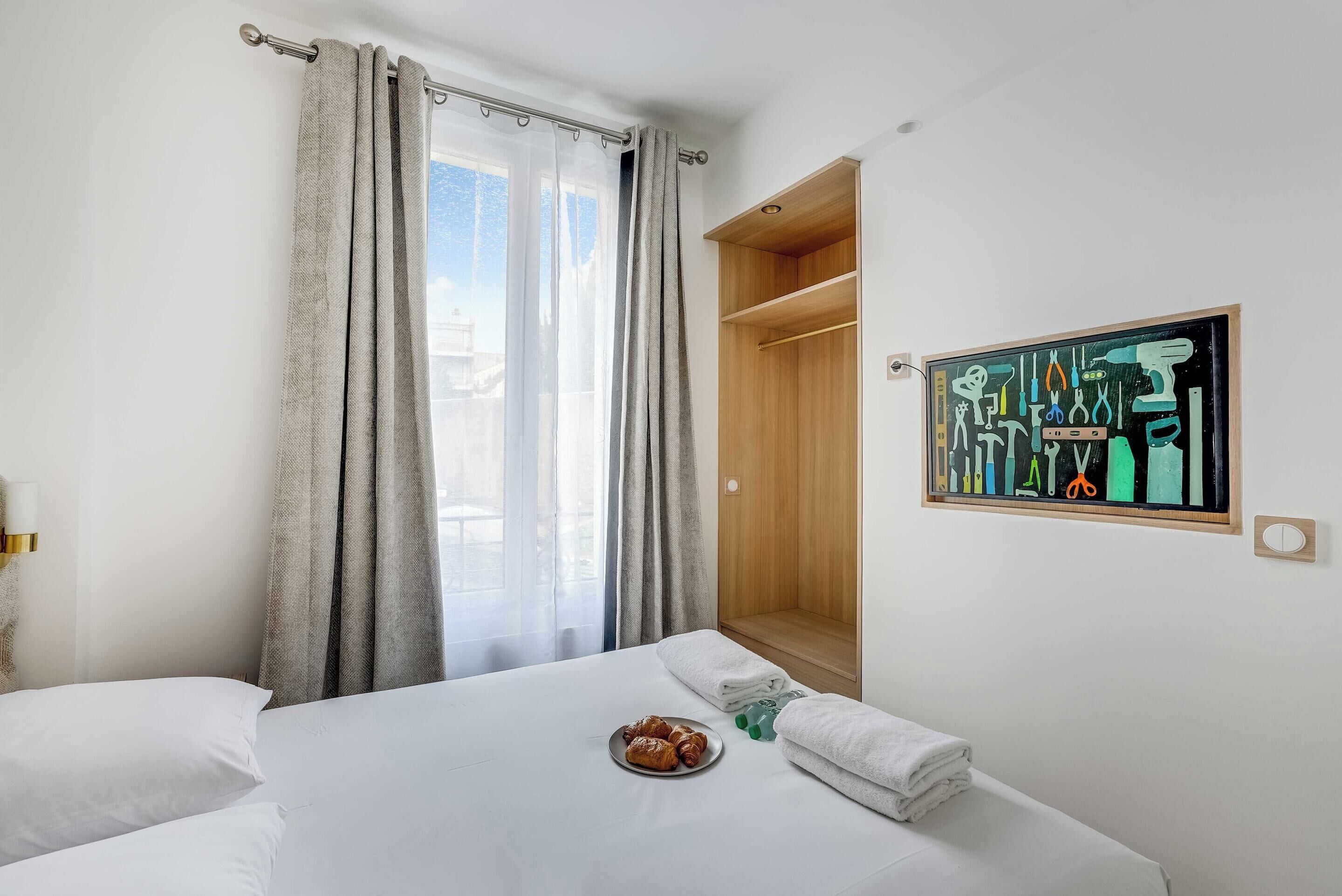 Habitación de hotel con una cama, una mesita de noche con un plato de pasteles, un armario y un cuadro en la pared.