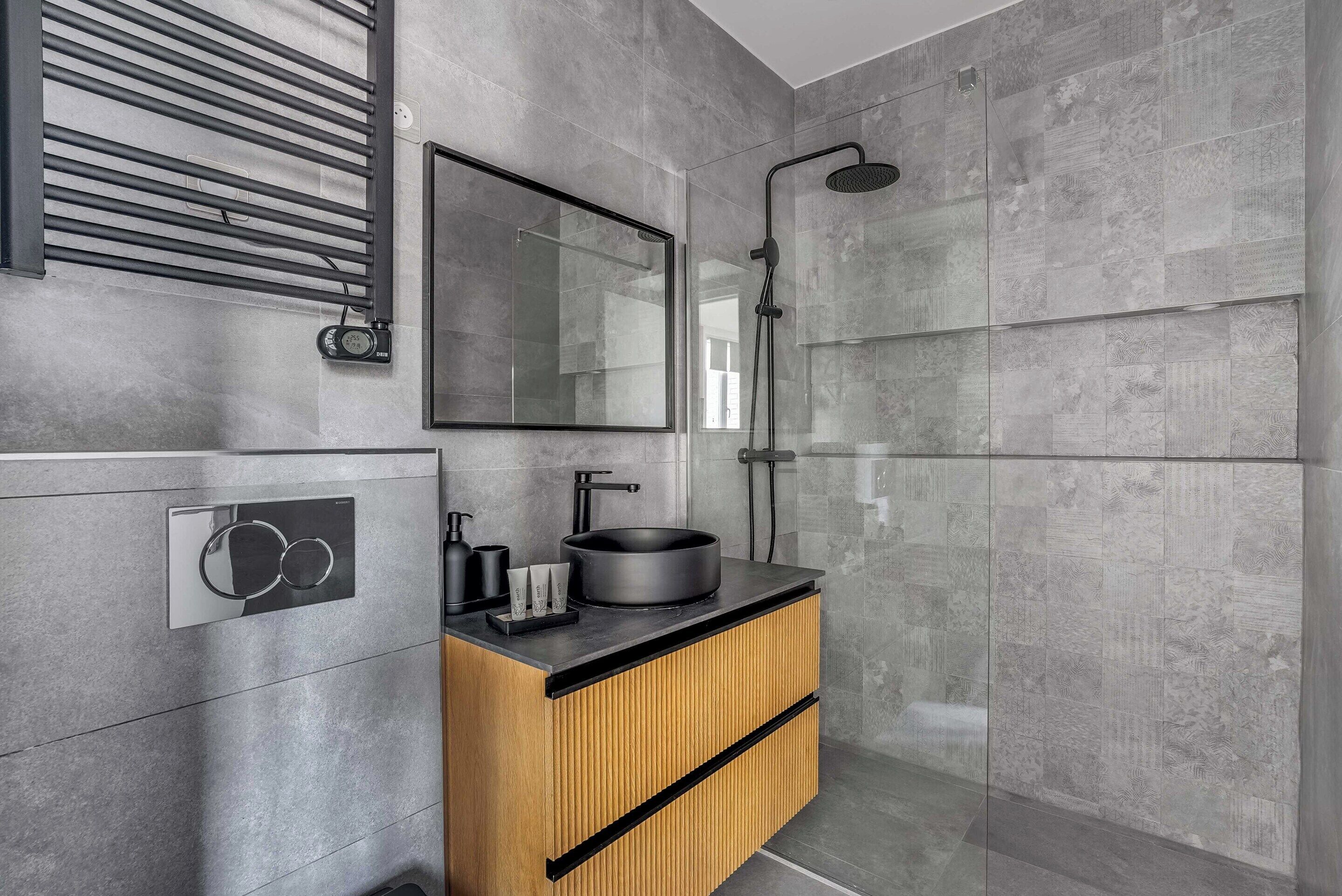 Un baño moderno con cabina de ducha de vidrio, tocador de madera con lavabo negro y un espejo grande.