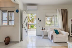 Ein Zimmer mit einem weißen Sofa, einem kleinen Tisch und einem Balkon mit Blick auf Palmen.