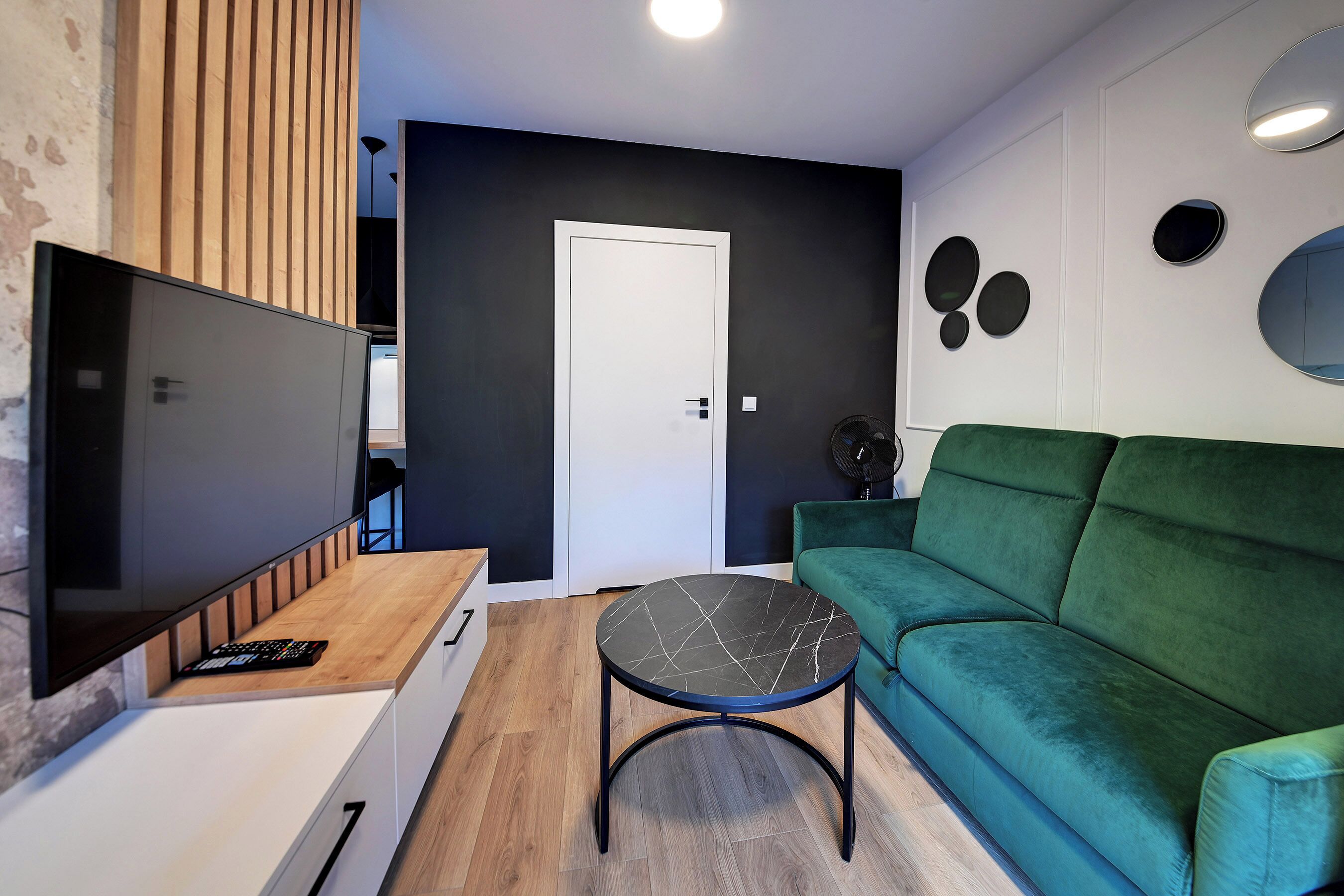 Una sala de estar moderna con un televisor de pantalla plana, un sofá verde, una mesa de centro redonda y una pared de acento de madera.