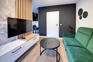 Un saló modern amb un televisor de pantalla plana, un sofà verd, una taula rodona i un moble de bany de fusta.