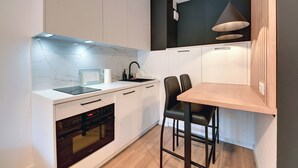 Una cocina moderna con armarios blancos, horno empotrado, pileta y comedor con mesa de madera y sillas negras.